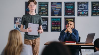Picture shows a young boy standing up and speaking in class as the teacher watches with pride.