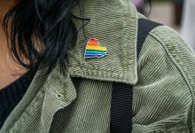 green jacket collar close up of a rainbow heart gay queer pin