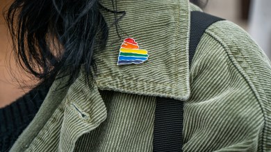 green jacket collar close up of a rainbow heart gay queer pin