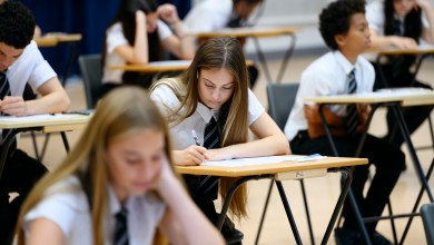 Teenage girl wearing school shirt and tie writing in exam booklet, arm resting on desk