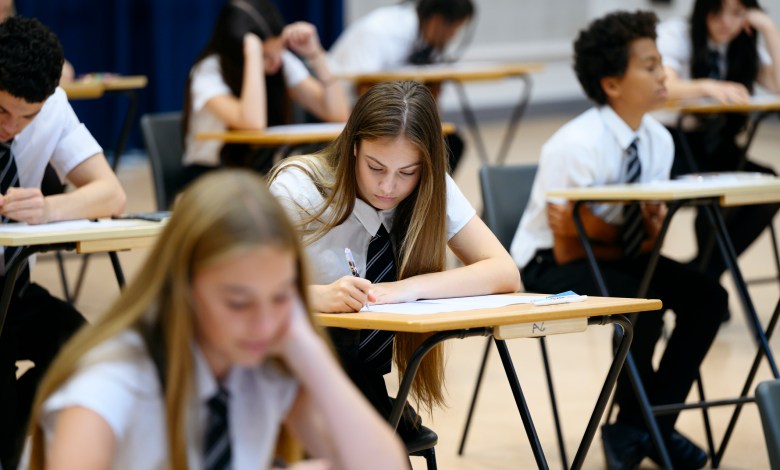 Teenage girl wearing school shirt and tie writing in exam booklet, arm resting on desk