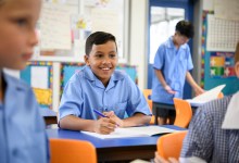 School boy wearing blue shirt listening in class with cheerful expression