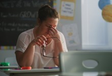 Tired Female Teacher Sitting Alone at the Desk in Empty Classroom, Relaxing After Class. Woman Feeling Stress, Burnout and Mental Exhaustion in Educational Environment, Working in Elementary School.
